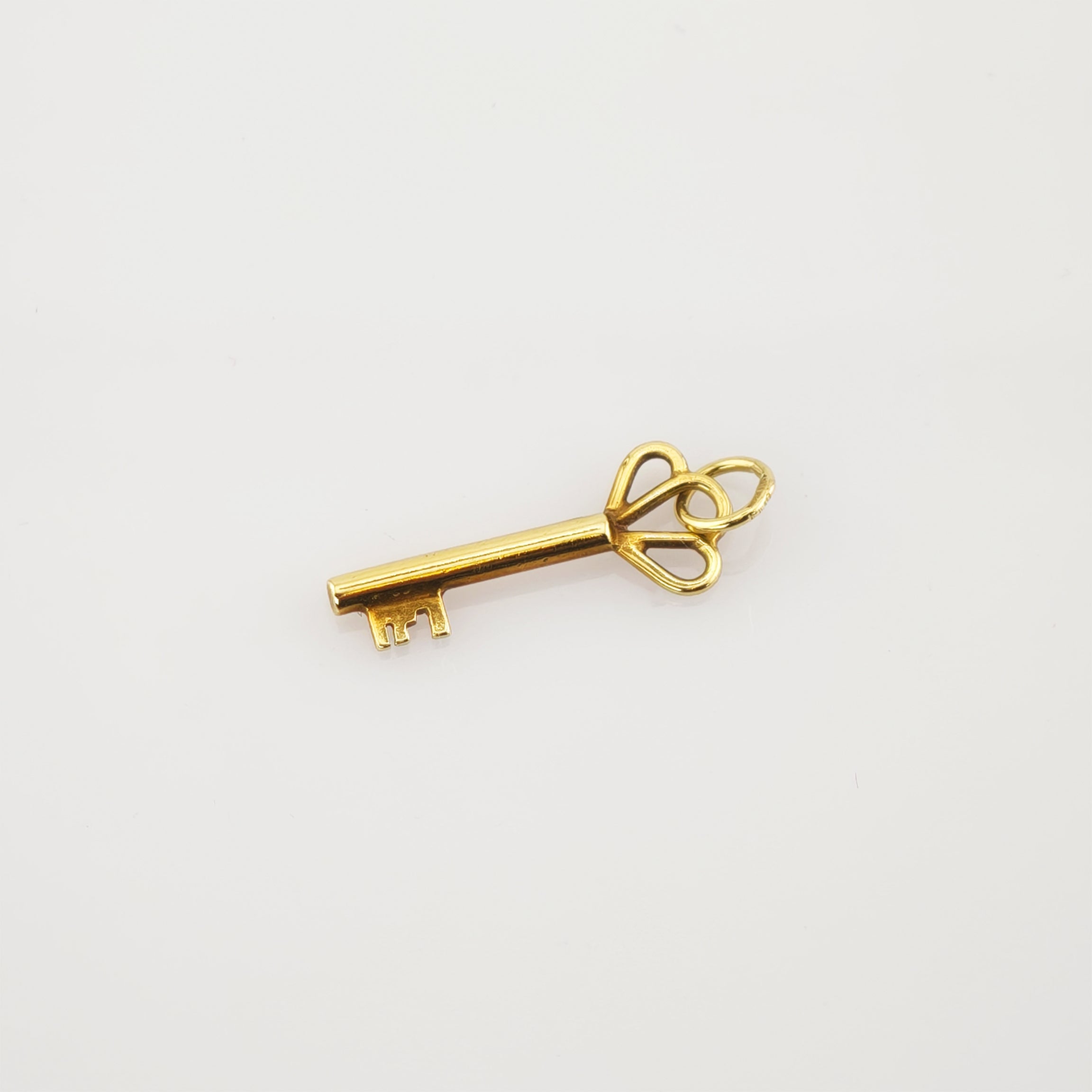 Kleiner goldener Schlüssel mit verziertem Bogen und Schleife auf weißem Hintergrund.