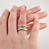 Linke Hand mit breitem goldenen BVLGARI-Ring mit Diamanten, rechte Hand hält die Finger, beide mit nude Nagellack.