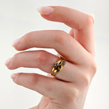 Linke Hand mit Goldring am Mittelfinger, drei ovale Steine in Schwarz, Klar und Rot