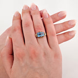 Linke Hand mit Goldring und rechteckigem blauem Edelstein auf dem Ringfinger, gepflegte natürliche Fingernägel.