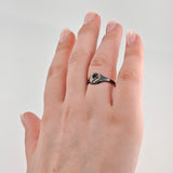 Linke Hand mit gepflegten Nägeln und schwarzem Metallschildring mit Kreuz und Streifen.