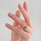 Linke Hand mit silbernem Ring mit Zweiblattdesign am Ringfinger vor neutralem Hintergrund.