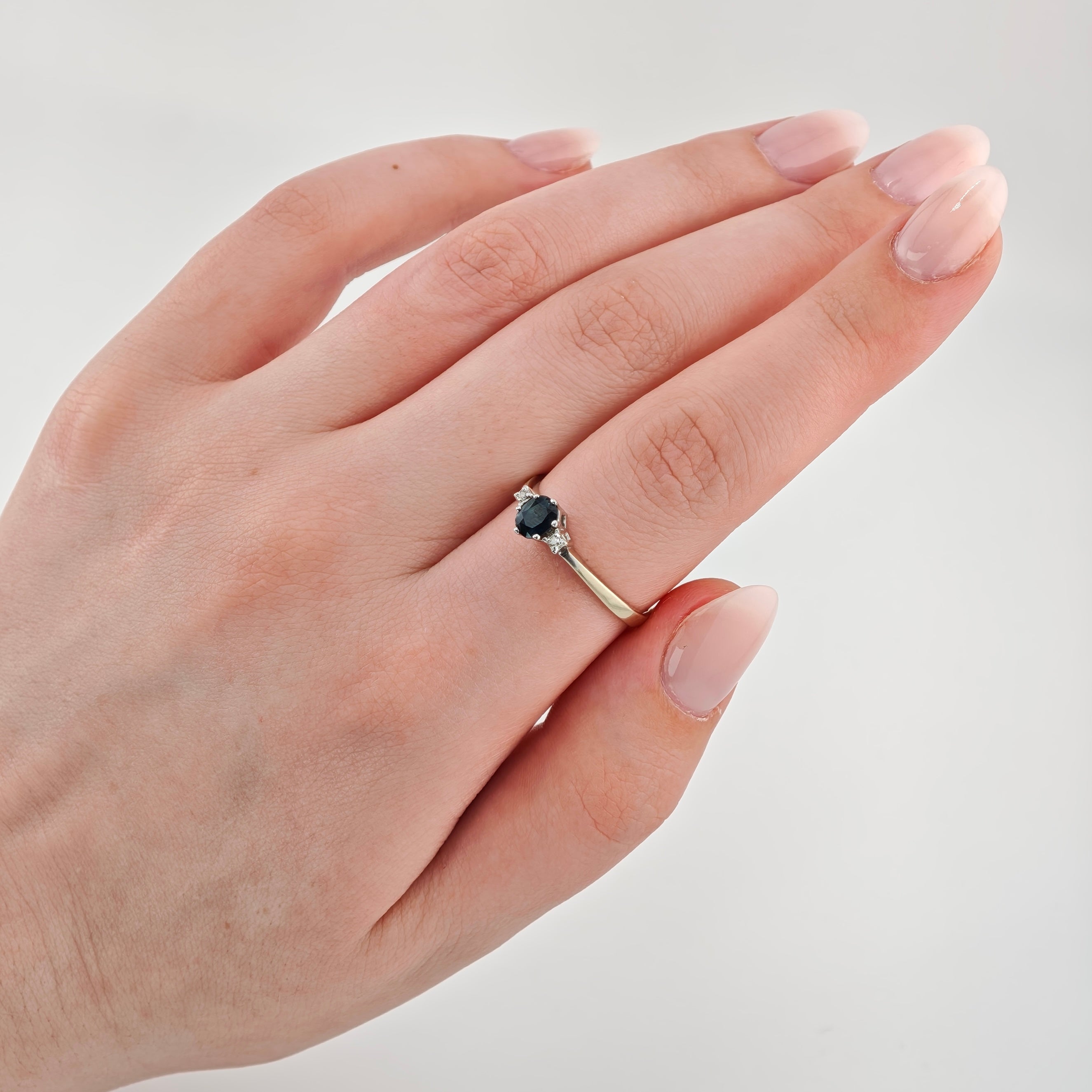 Linke Hand mit rosa lackierten Nägeln, trägt silbernen Ring mit ovalem Schmuckstein.