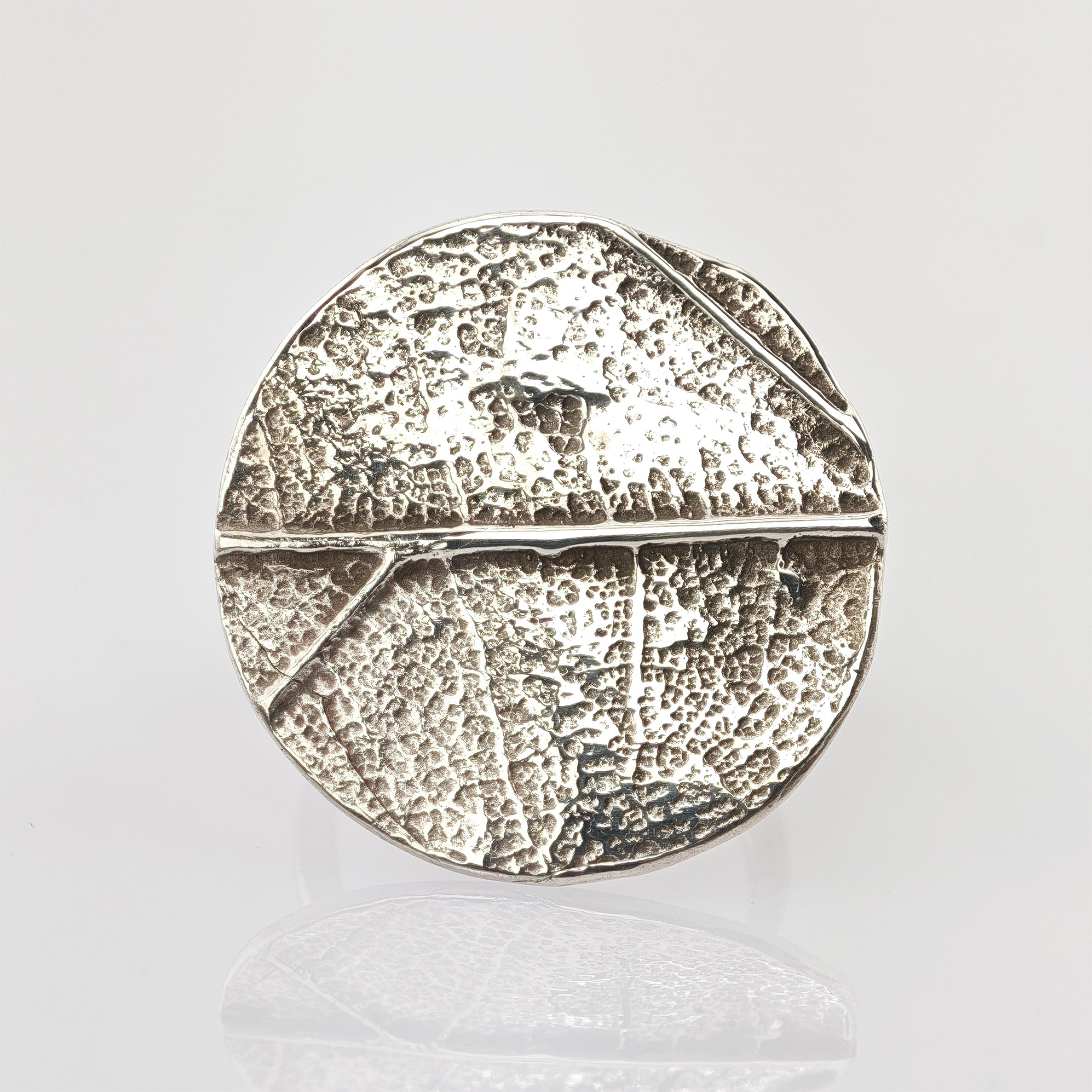 Metallisches Objekt mit strukturierter, rissiger Oberfläche, unterteilt in Segmente, mit glänzendem Silberfinish