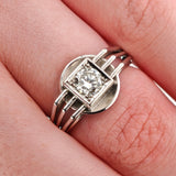 Nahaufnahme einer Hand mit silbernem Ring, geometrischem Design und Diamanten in quadratischem Rahmen.