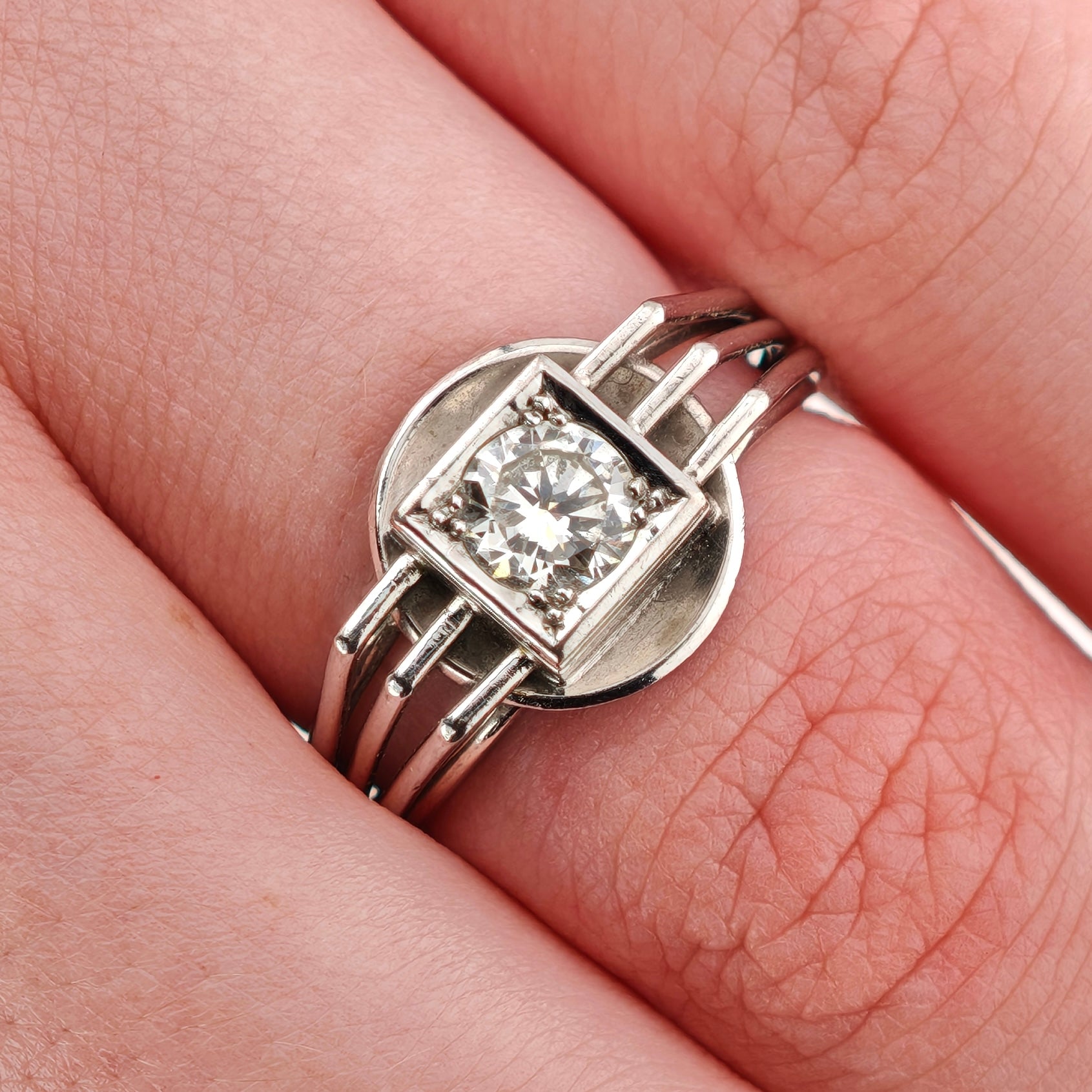 Nahaufnahme einer Hand mit silbernem Ring, geometrischem Design und Diamanten in quadratischem Rahmen.