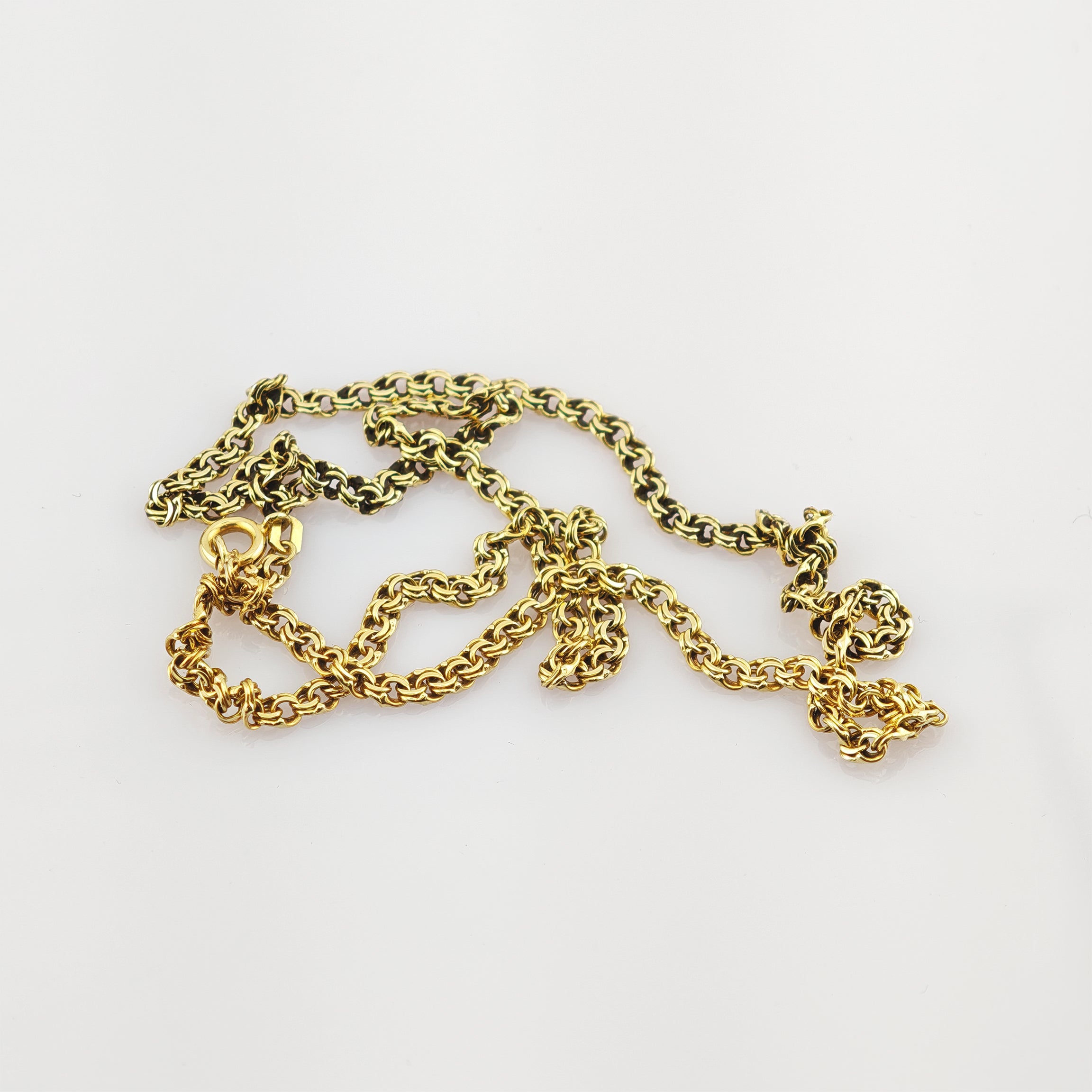 Nahaufnahme einer verhedderten goldenen Kette mit ovalen Gliedern auf weißem Hintergrund.