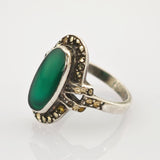 Ornater Vintage-Silberring mit großem ovalem grünen Stein und kleinen Gold-Silber-Verzierungen im dekorativen Rahmen.