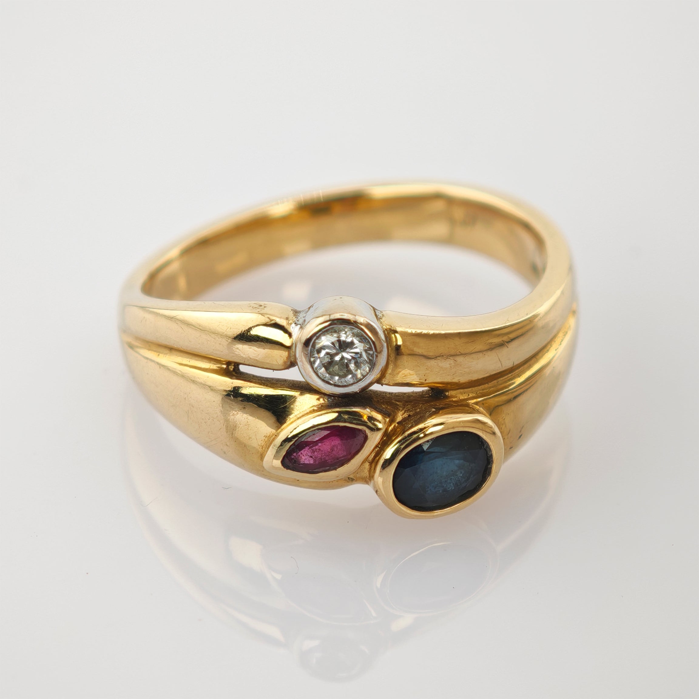 Ein polierter Goldring mit Diamant, Rubin und Saphir auf weißem Hintergrund.