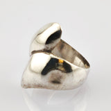 Polierter Metallschmuckring mit abstrakter, asymmetrischer Form auf weißem Hintergrund.