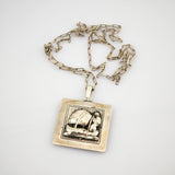 Quadratischer silberner Anhänger mit Gravur einer Person neben einem Segelboot an Kette mit rechteckigen Gliedern