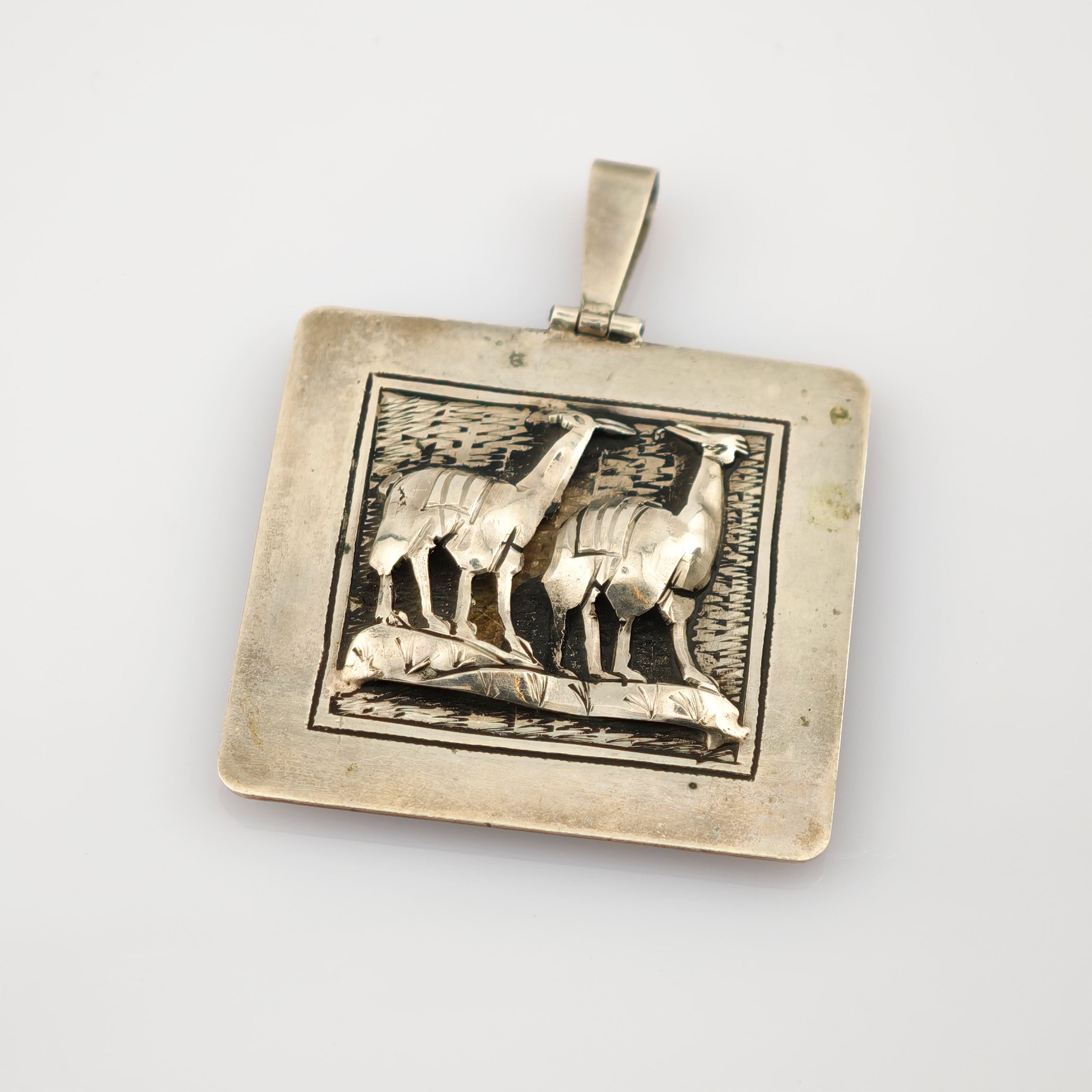 Quadratischer silberfarbener Anhänger mit Reliefdarstellung von zwei Llamas und feiner Gravur.