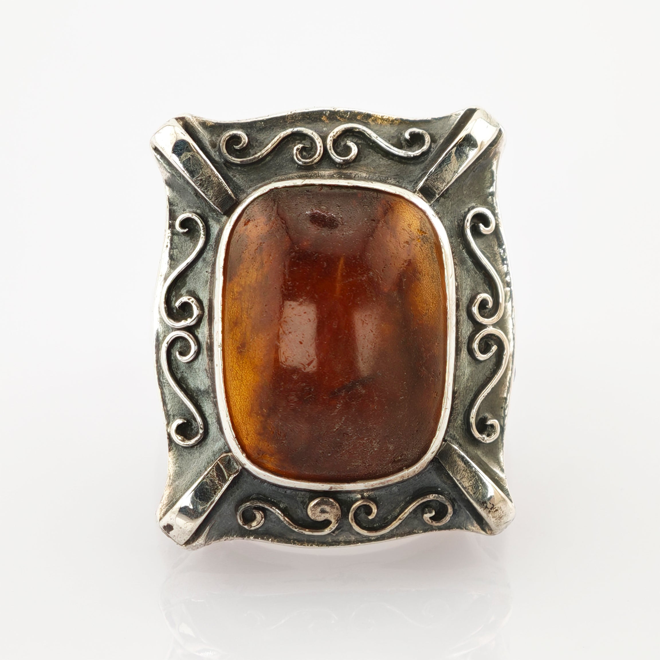 Rechteckiger Vintage-Ring mit poliertem braunem Bernstein und silbernem Rahmen mit Wirbelmustern.