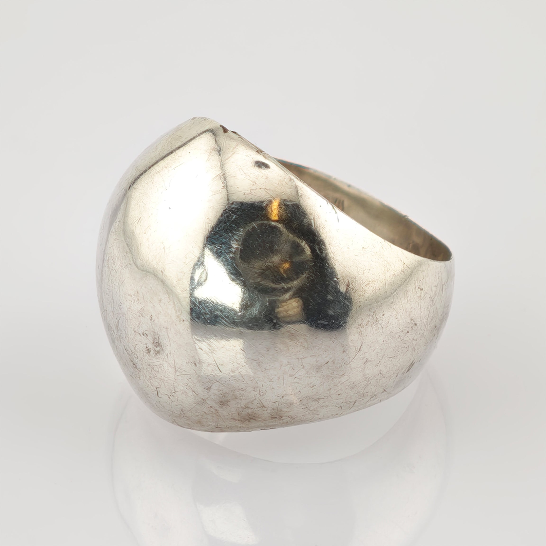 Reflektierender Metallring mit abgenutzter Oberfläche und Kratzern vor hellgrauem Hintergrund