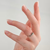 Hand mit hellrosa lackierten, mandelförmigen Nägeln und einem silbernen Ring mit kleinen Edelsteinen.