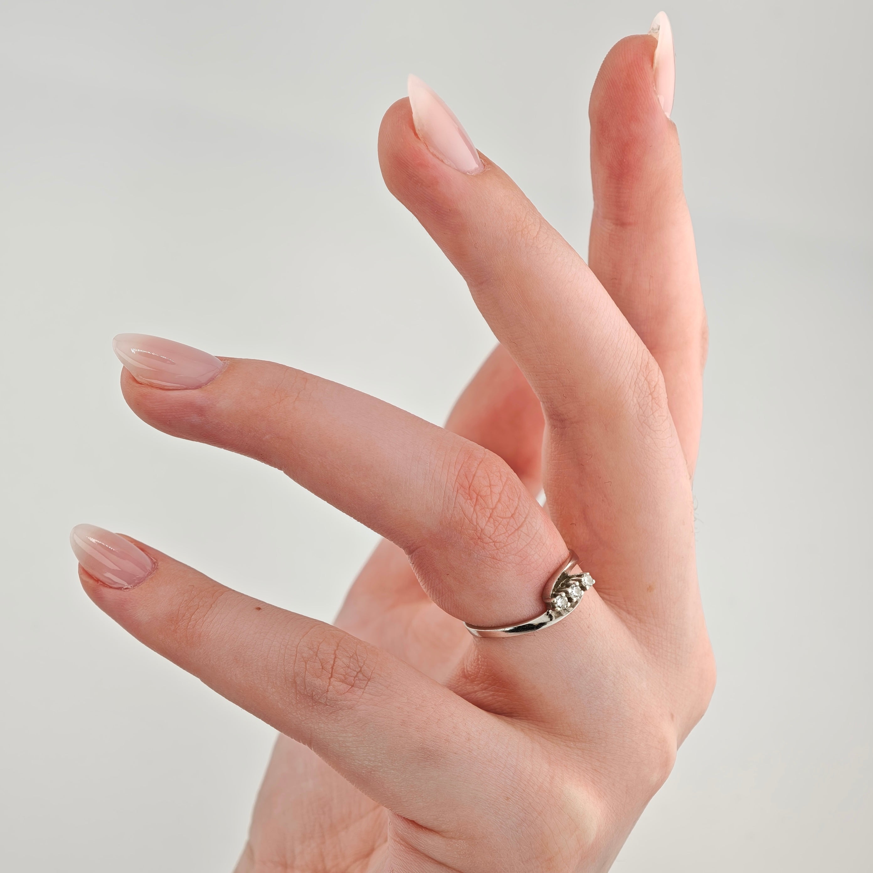Hand mit hellrosa lackierten, mandelförmigen Nägeln und einem silbernen Ring mit kleinen Edelsteinen.