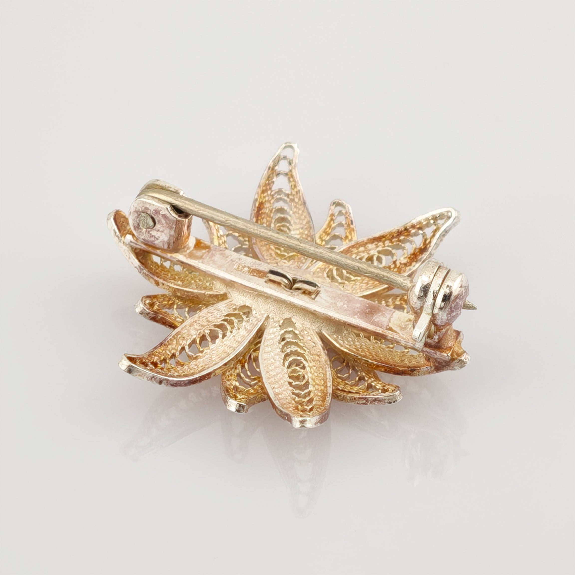 Rückseite einer goldfarbenen Blumenbrosche mit filigranem Metalldesign und Sicherheitsverschluss.