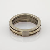 Zweiseitiger Metallring mit silbernem Außenband und goldenem Innenband auf reflektierender Oberfläche