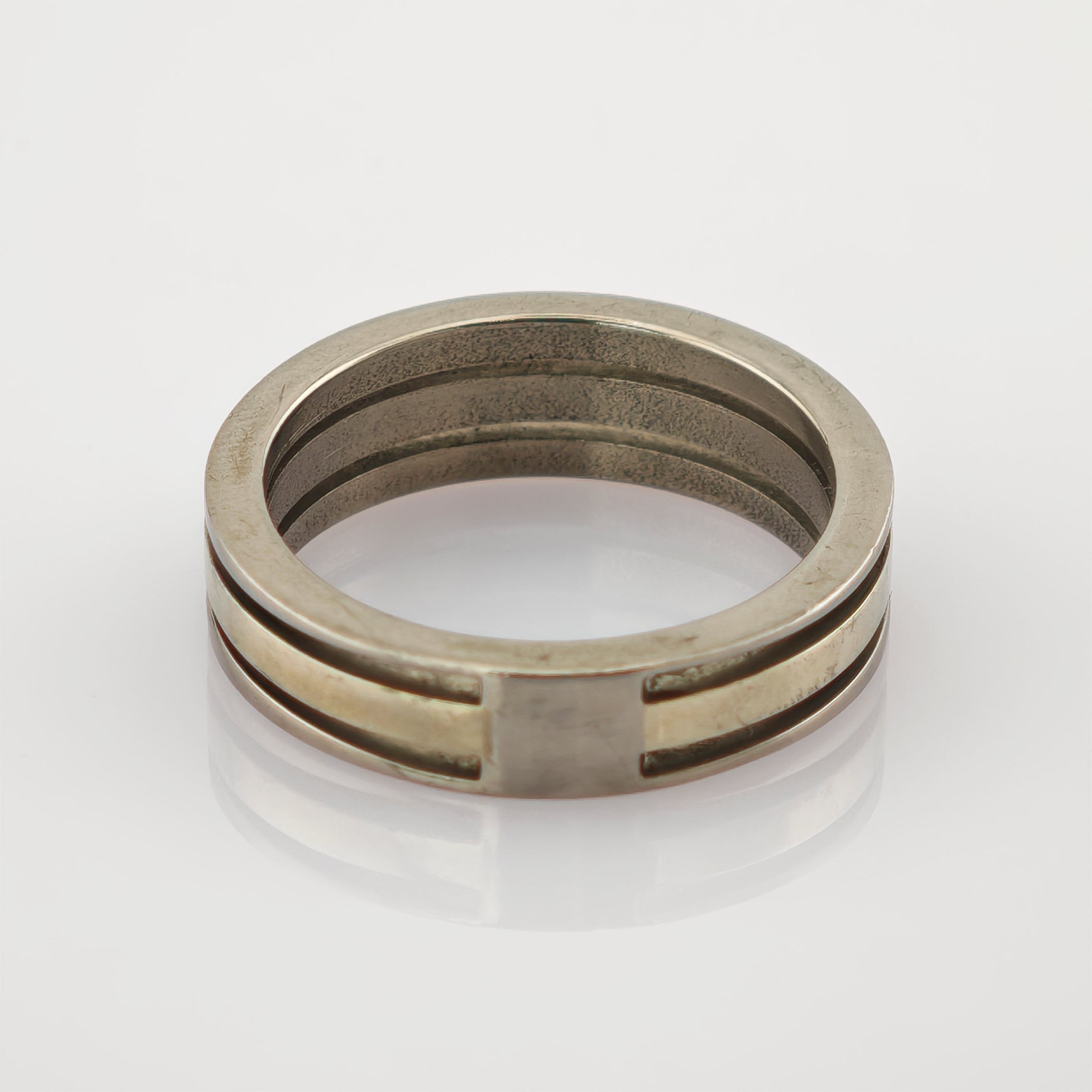 Zweiseitiger Metallring mit silbernem Außenband und goldenem Innenband auf reflektierender Oberfläche