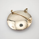 Rückseite eines runden, silberfarbenen Schmuckstücks mit halbmondförmigem Rand und Stempel 900.