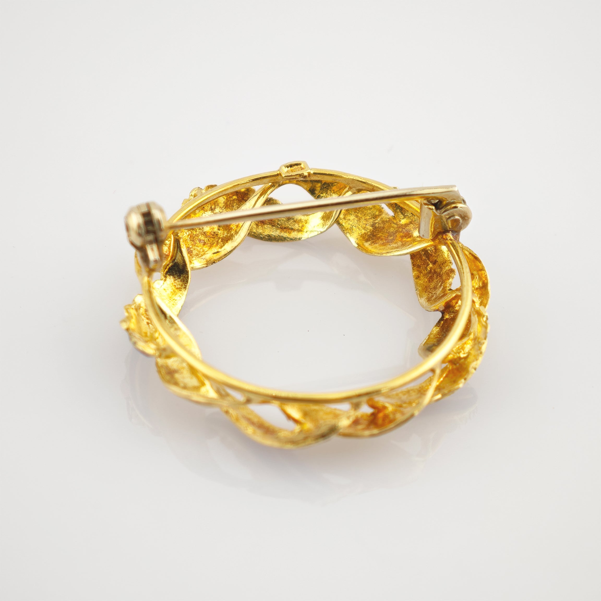 Runde Goldbrosche mit Blattrankenmuster und Nadelverschluss auf glatter Oberfläche