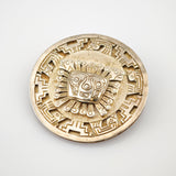 Rundes Metallmedaillon mit detaillierten Gravuren und stilisiertem Gesicht in der Mitte.