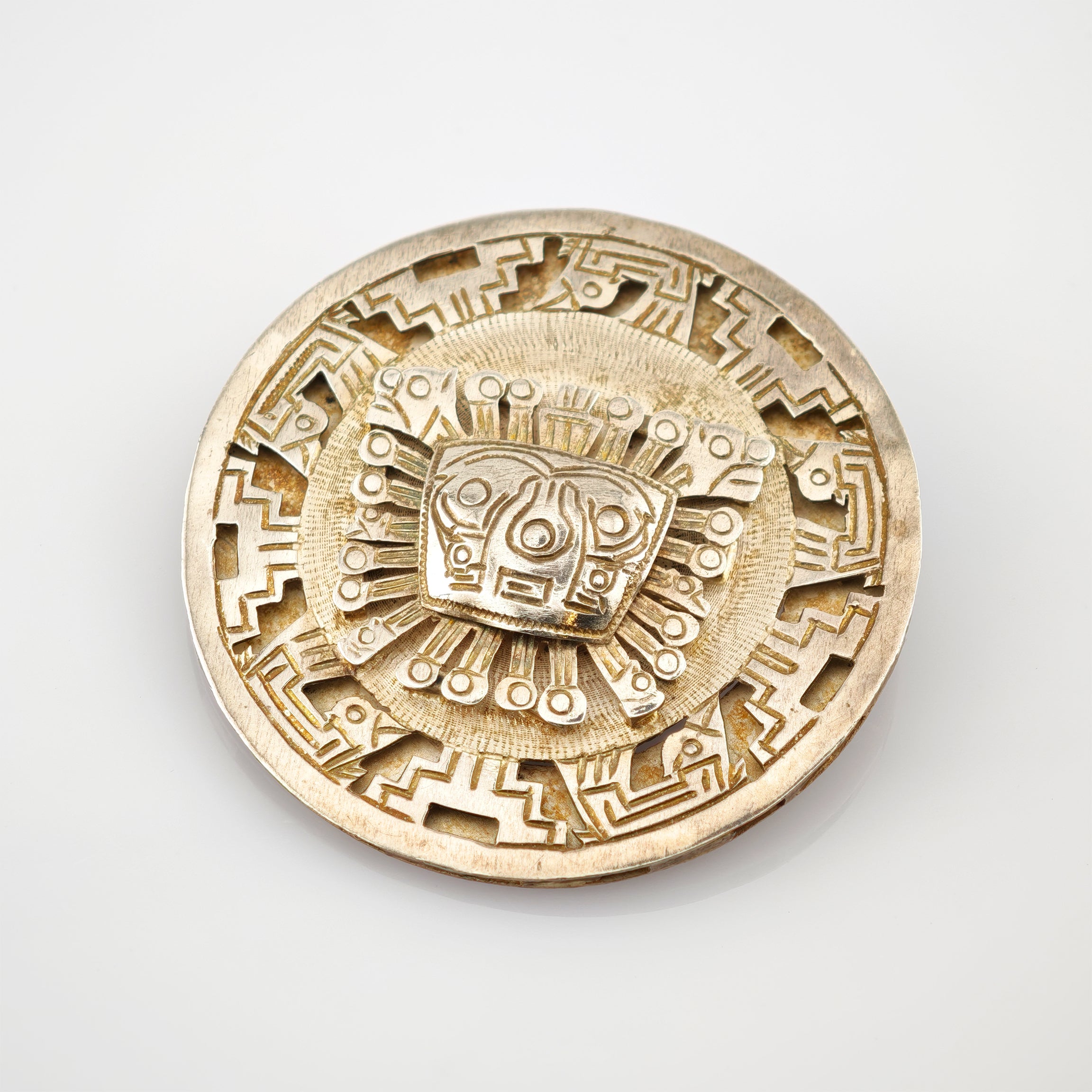 Rundes Metallmedaillon mit detaillierten Gravuren und stilisiertem Gesicht in der Mitte.