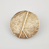 Rundes metallisches Objekt mit Blattaderstruktur in Gold und Bronze mit gealterter Patina.