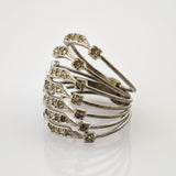 Schlichter Silberring mit fächerförmigem Design und kleinen klaren Edelsteinen auf hellem, reflektierendem Untergrund.