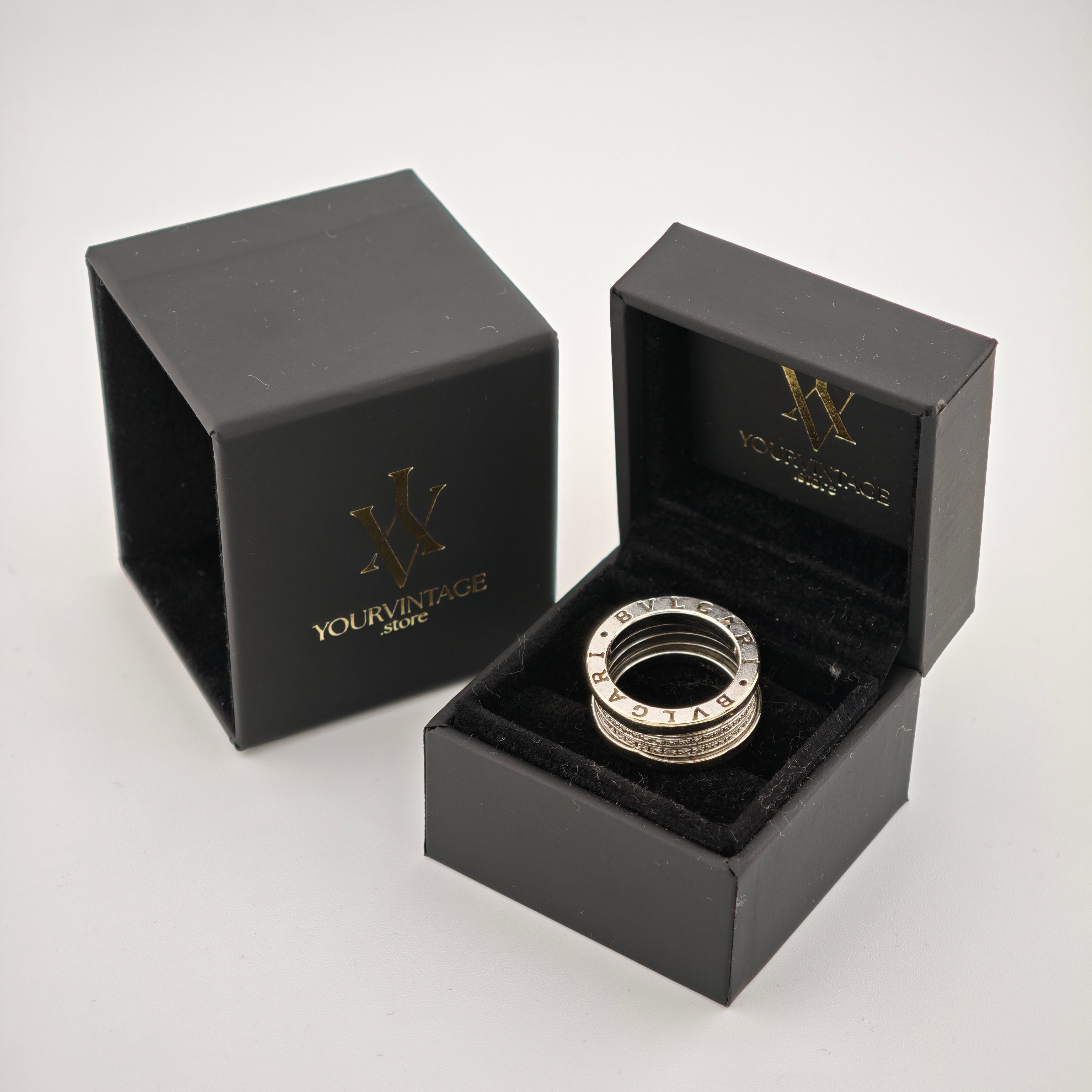 Zwei schwarze Schmuckboxen mit goldener Aufschrift "YOURVINTAGE.store" und stilisiertem W-Logo. Eine Box zeigt einen silbernen BVLGARI-Ring auf schwarzem Samtkissen.