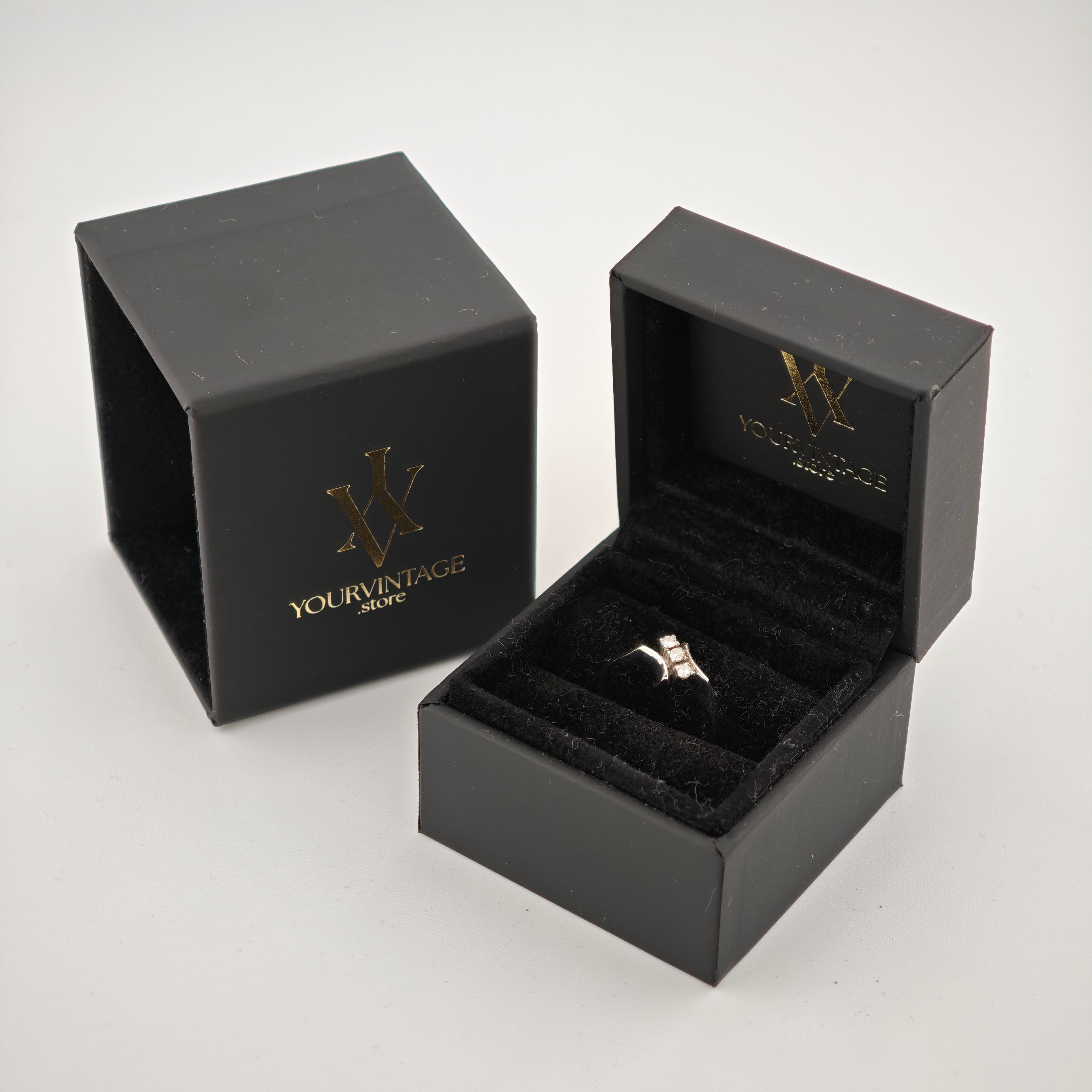 Geöffnete schwarze Schmuckbox mit Silberring und drei quadratischen Steinen, daneben geschlossene Box mit "YourVintage Store" Goldprägung.