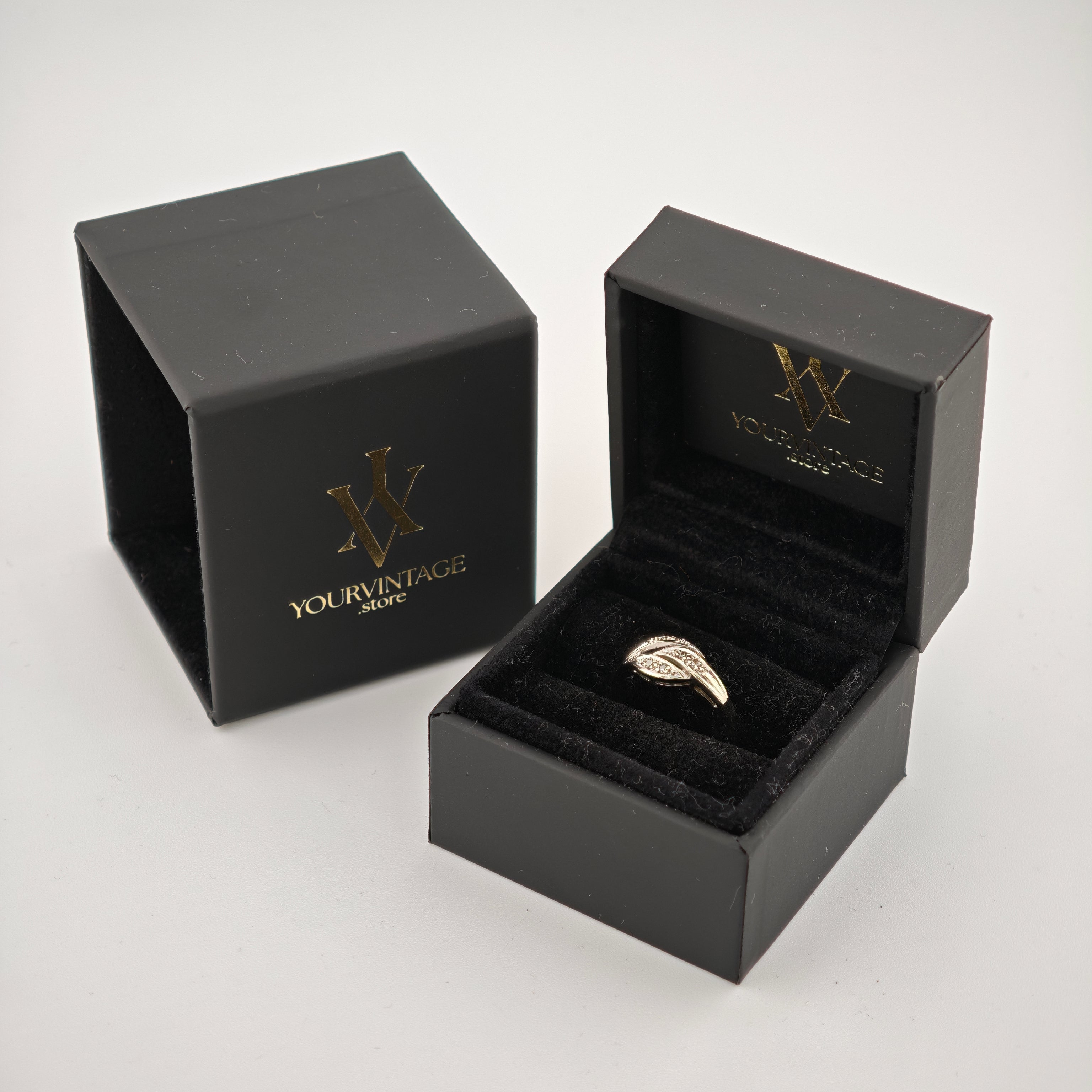 Zwei elegante schwarze Ringboxen, eine offen mit einem silbernen Ring in Blattform auf schwarzem Samt, die andere geschlossen mit goldgeprägtem YOURVINTAGE.store Logo.