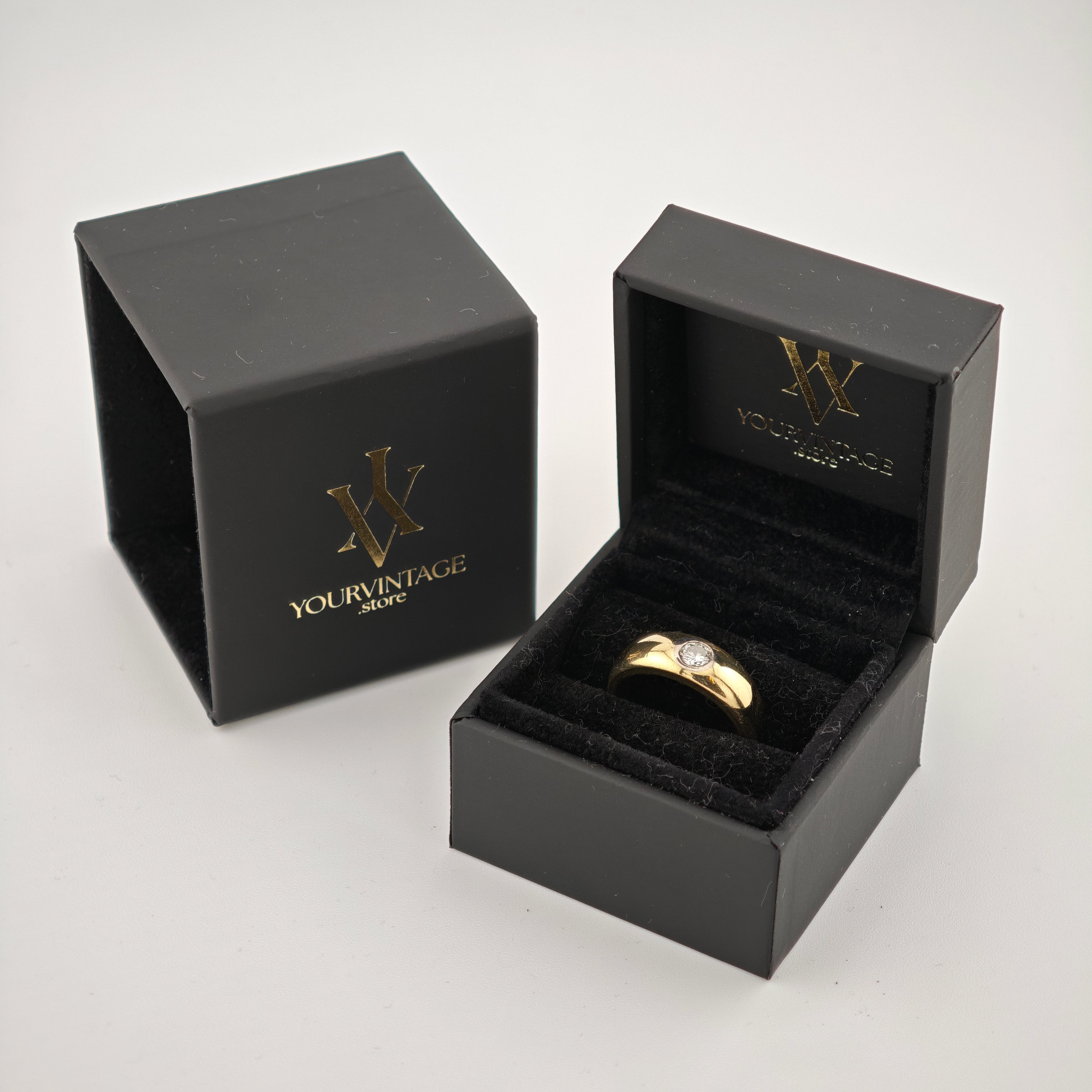Zwei schwarze Schmuckboxen mit goldfarbenem YOURVINTAGE.store Logo, eine geöffnet mit goldenem Ring und klarem Edelstein.