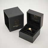 Schwarze Schmuckkästchen mit goldener Signatur und offenem Kästchen, das einen goldenen Ring mit klarem Edelstein zeigt.