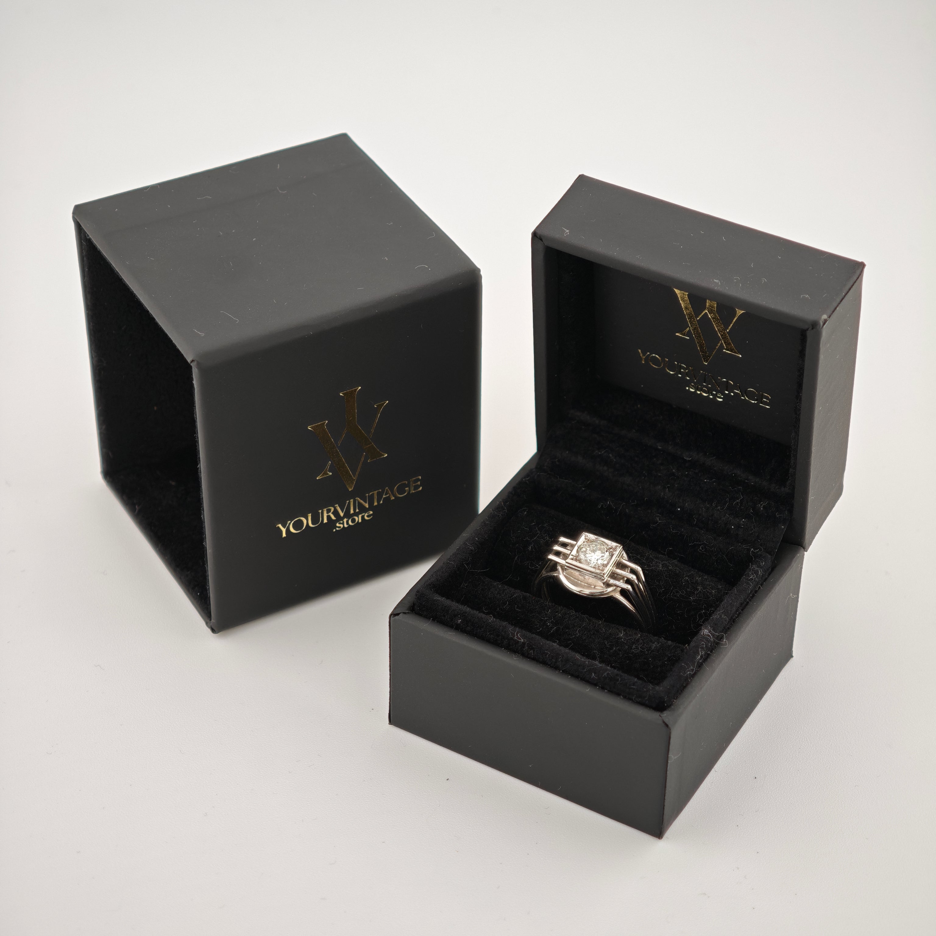 Zwei elegante schwarze Schmuckschatullen auf weißem Hintergrund, eine offen mit silbernem Ring und quadratischem Diamanten.