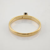 Seitliche Ansicht eines goldenen Rings mit kleinem Stein auf weißem reflektierendem Untergrund.