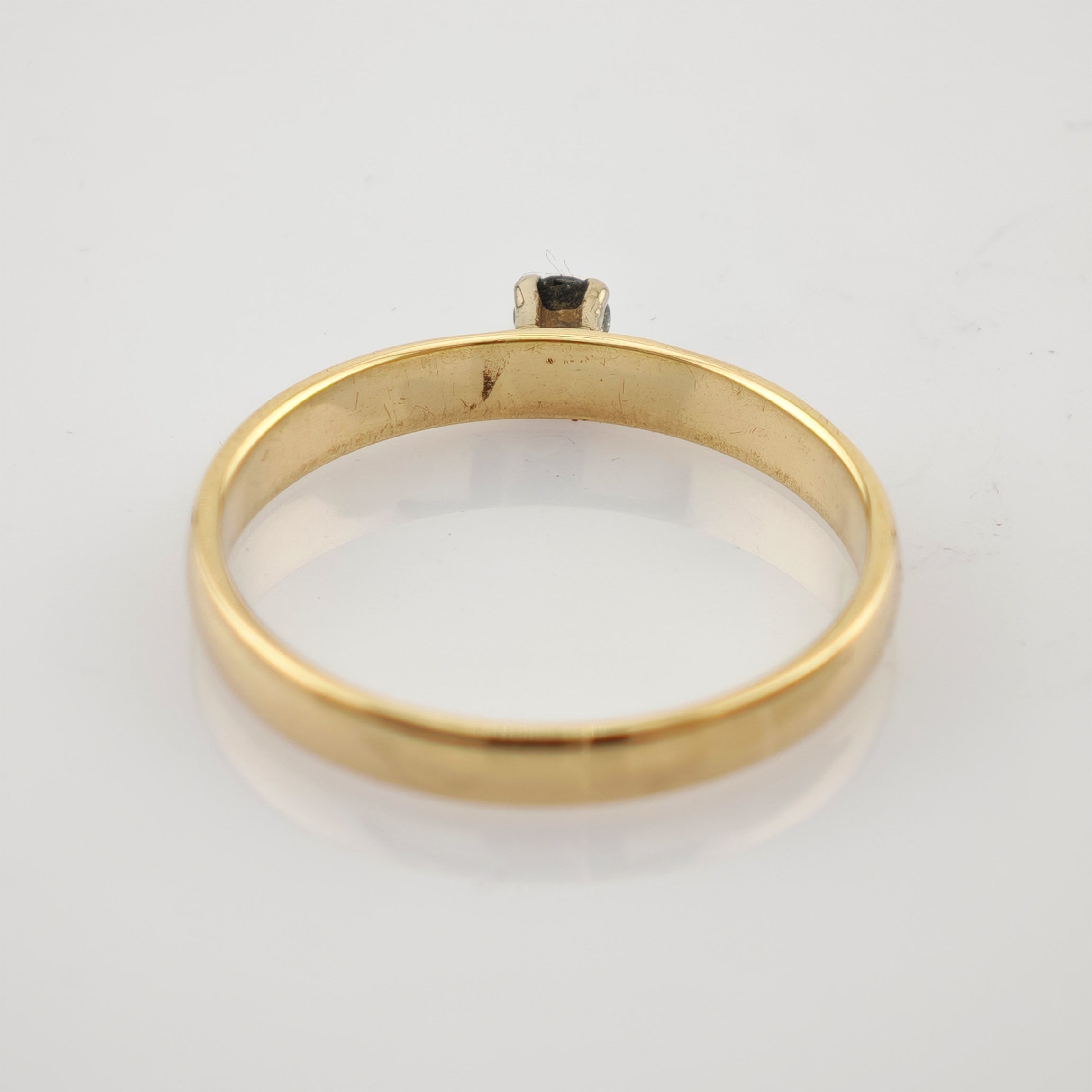 Seitliche Ansicht eines goldenen Rings mit kleinem Stein auf weißem reflektierendem Untergrund.