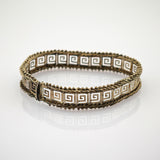 Silberarmband mit quadratischen Gliedern und weißem griechischem Schlüsselmotiv auf spiegelndem Untergrund.