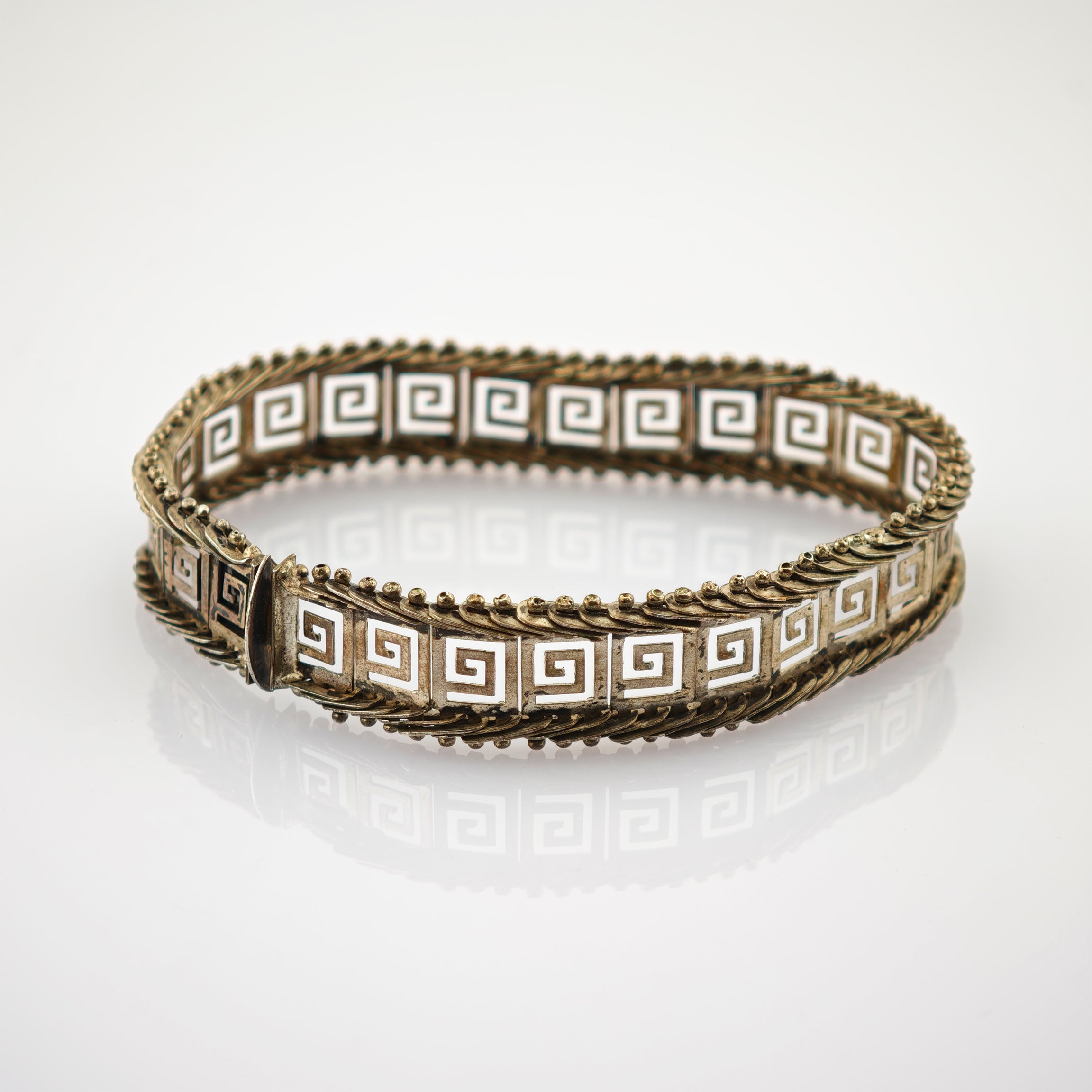 Silberarmband mit quadratischen Gliedern und weißem griechischem Schlüsselmotiv auf spiegelndem Untergrund.
