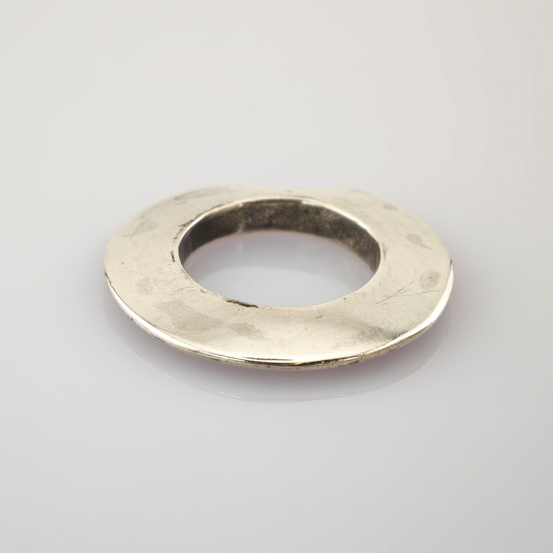 Silberne, abgenutzte Metallscheibe mit Loch in der Mitte auf hellem Hintergrund