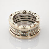 Detaillierte Nahaufnahme eines silberfarbenen Rings mit eingraviertem Bvlgari-Logo und 18K-Goldpunze auf reflektierender Oberfläche.