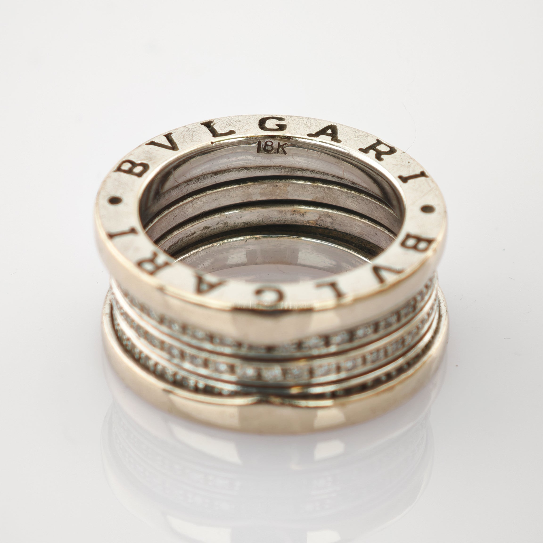 Detaillierte Nahaufnahme eines silberfarbenen Rings mit eingraviertem Bvlgari-Logo und 18K-Goldpunze auf reflektierender Oberfläche.