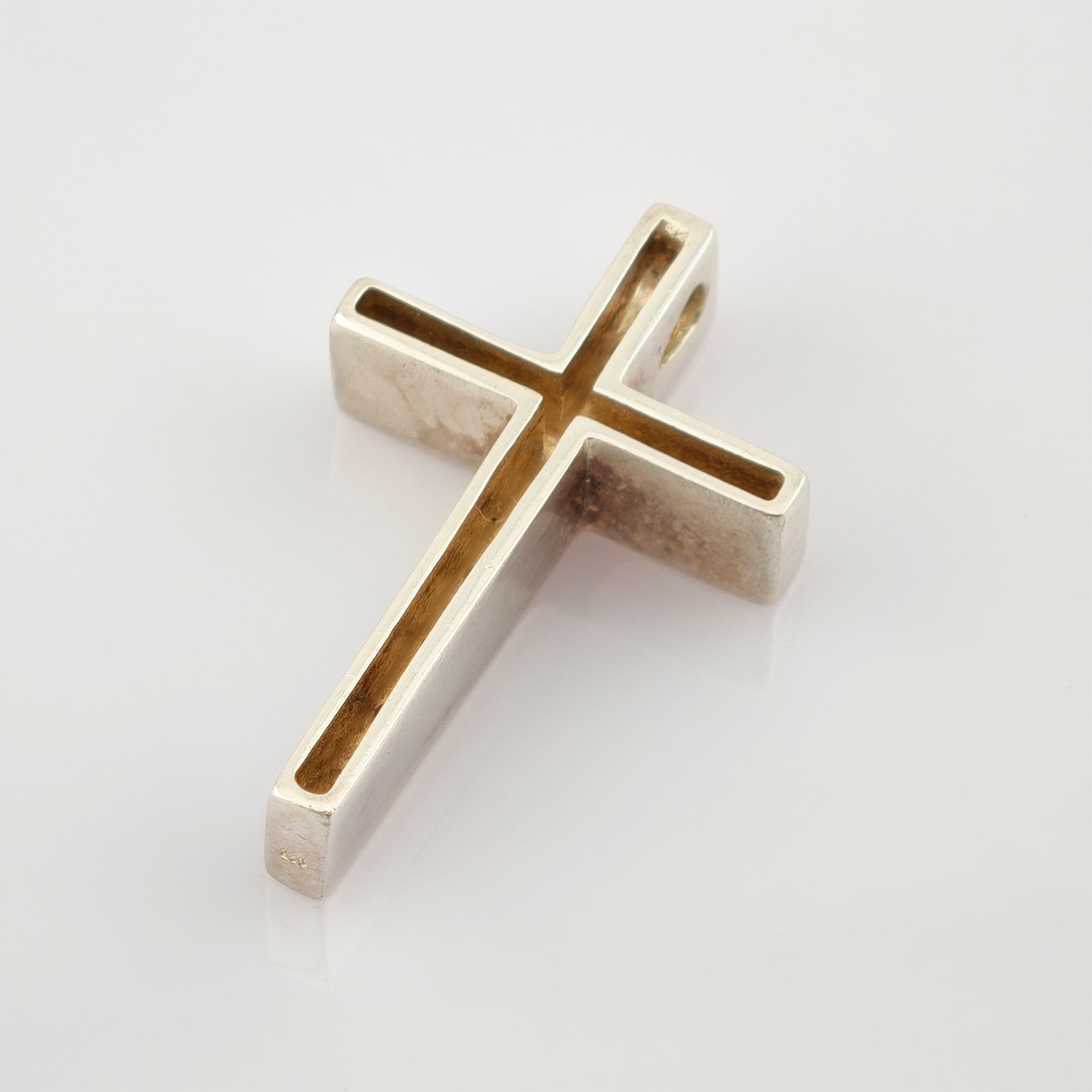 Silberner Kreuzanhänger mit hohlem Design auf glänzend weißem Untergrund.