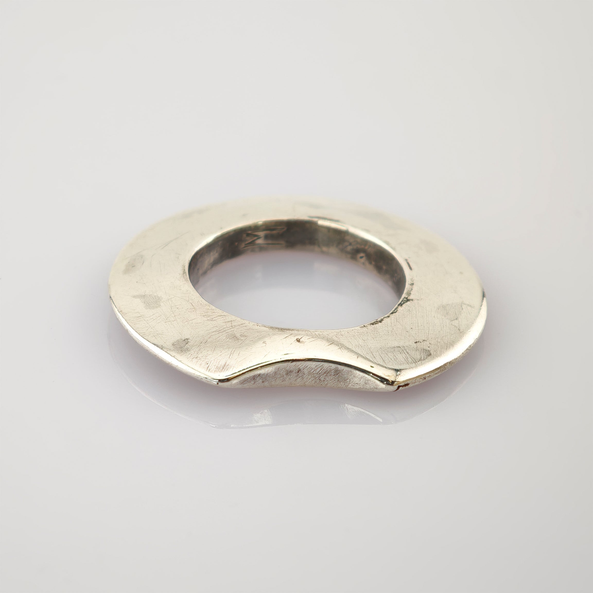 Silberner Ring mit abgeflachter, leicht welliger Bandform und sichtbaren Gebrauchsspuren auf reflektierender Oberfläche.