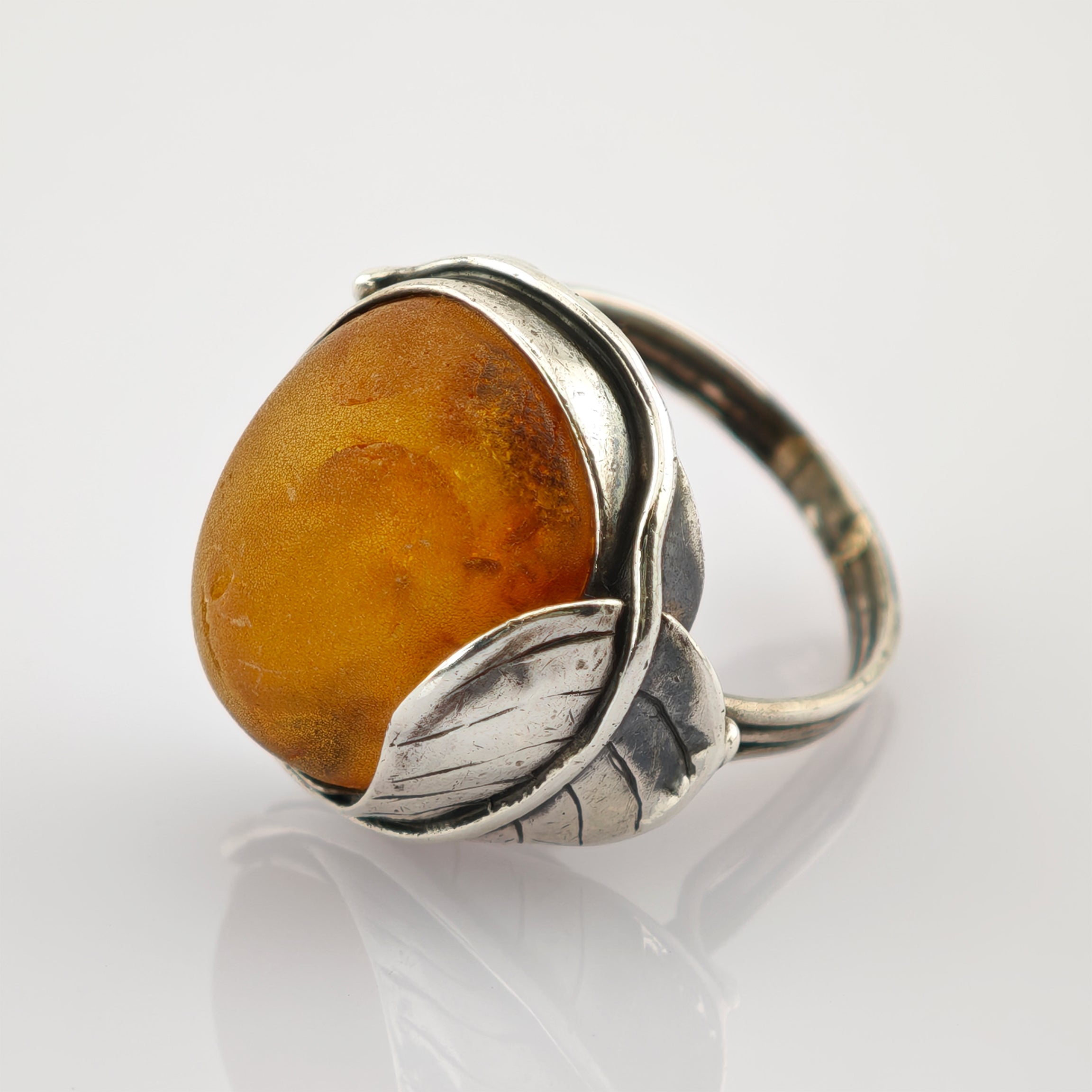 Silberner Ring mit großem rundem Bernstein und dekorativen silbernen Blättern.