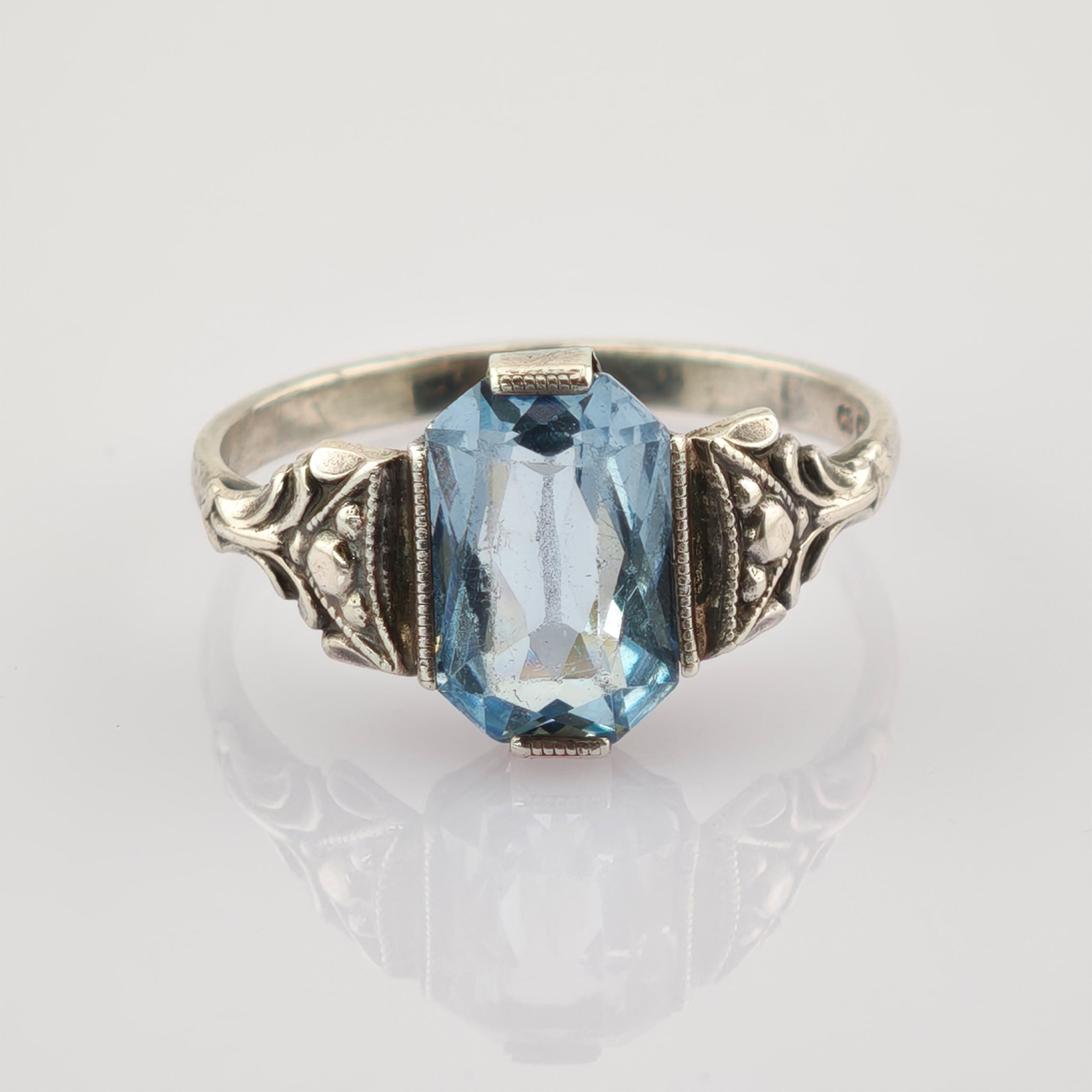 Eleganter silberner Ring mit blauem trapezförmigem Edelstein und floralen Verzierungen.