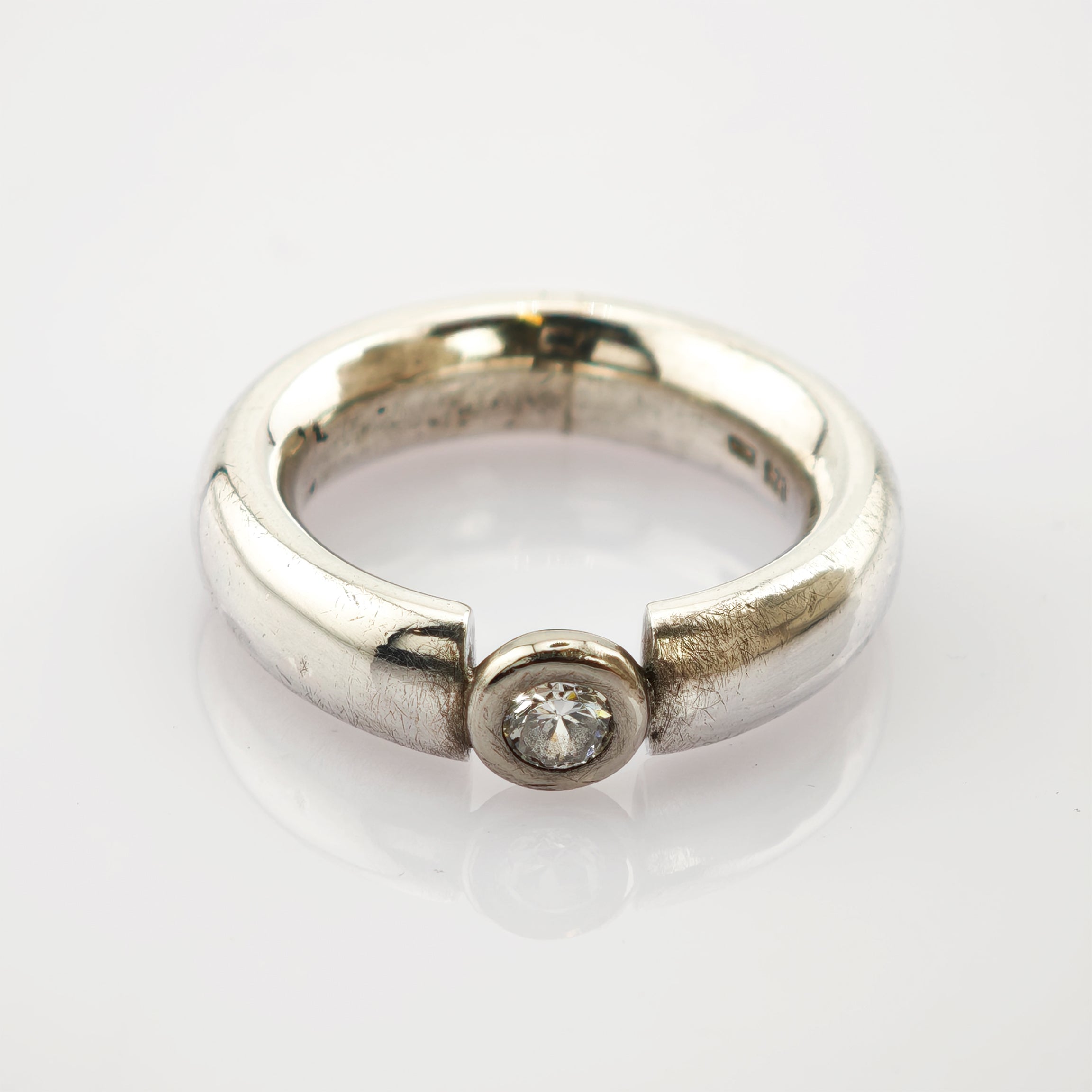 Silberner Ring mit breitem, offenem Band und einem runden Diamanten in Zargenfassung, minimalistisch und elegant.