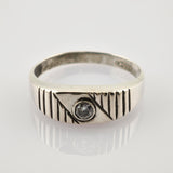 Silberner Ring mit diagonalen und vertikalen Gravuren und klarem Edelstein auf weißer Oberfläche