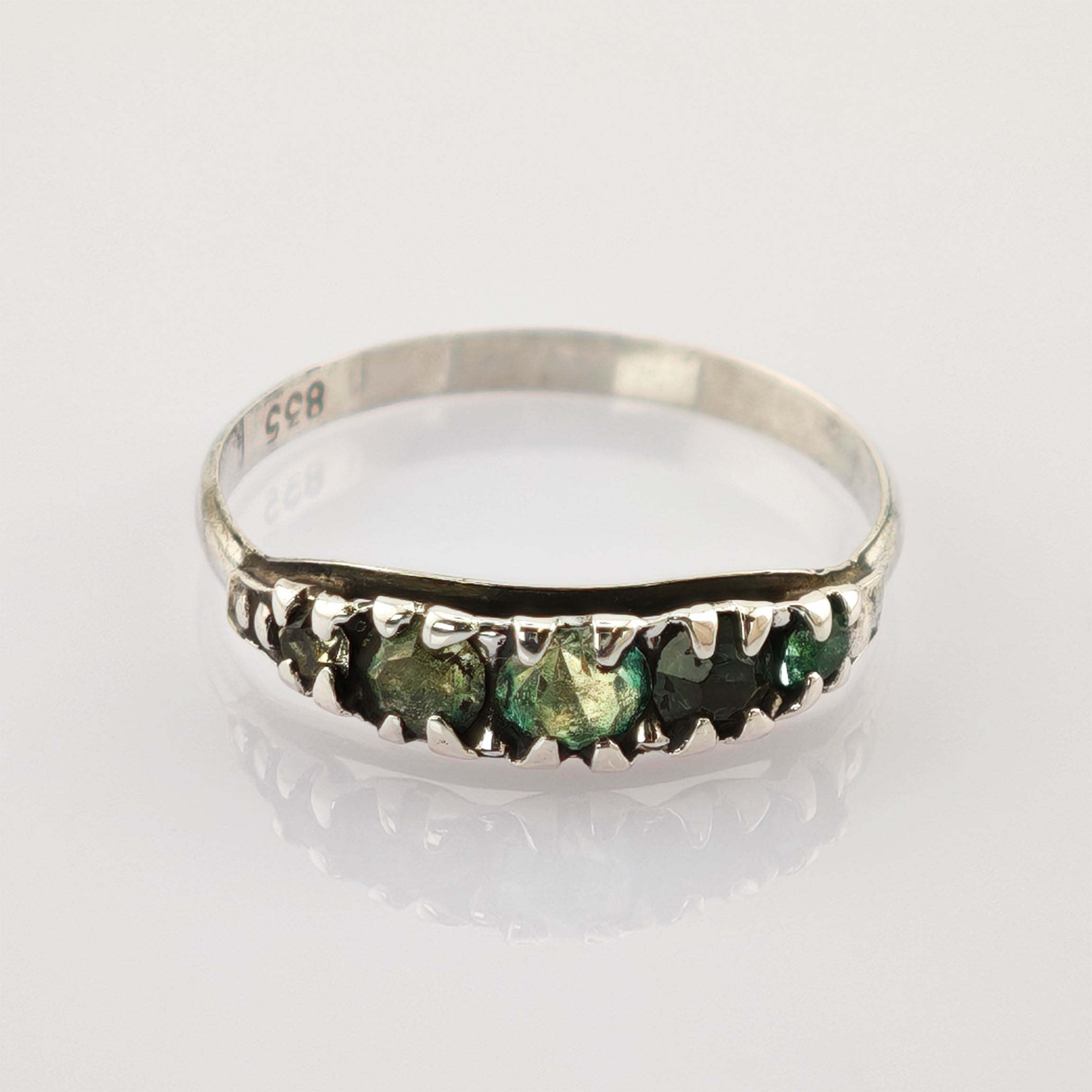 Silberner Ring mit fünf dunkelgrünen Steinen auf weißem reflektierendem Untergrund