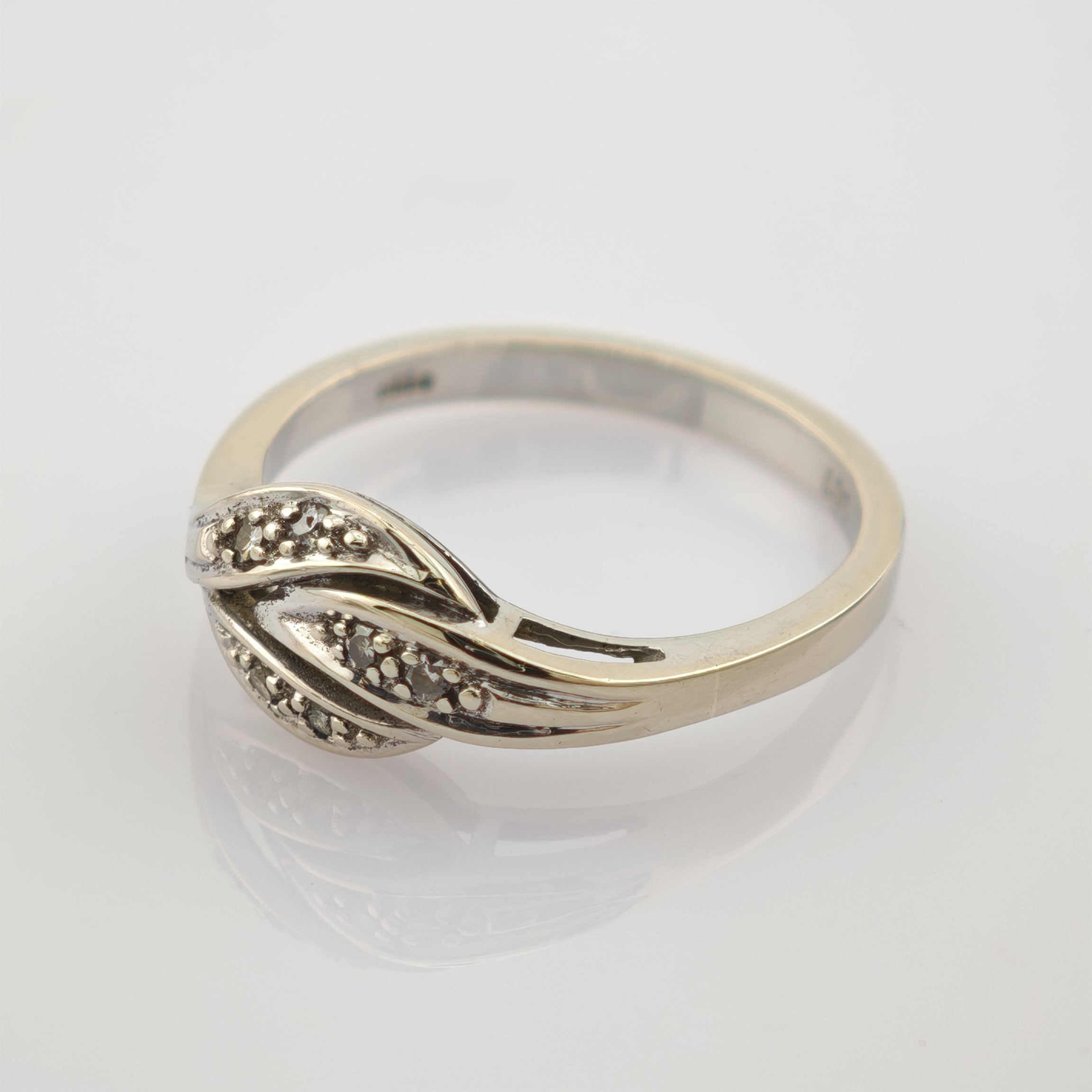 Silberner Ring mit geschwungenem Design und kleinen Steinclustern auf hellem reflektierendem Untergrund.